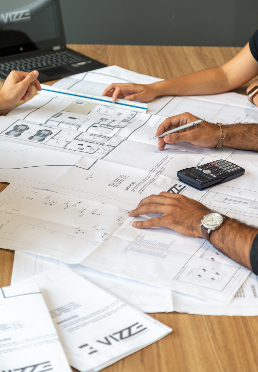 Three people reviewing blueprints on a wooden table.