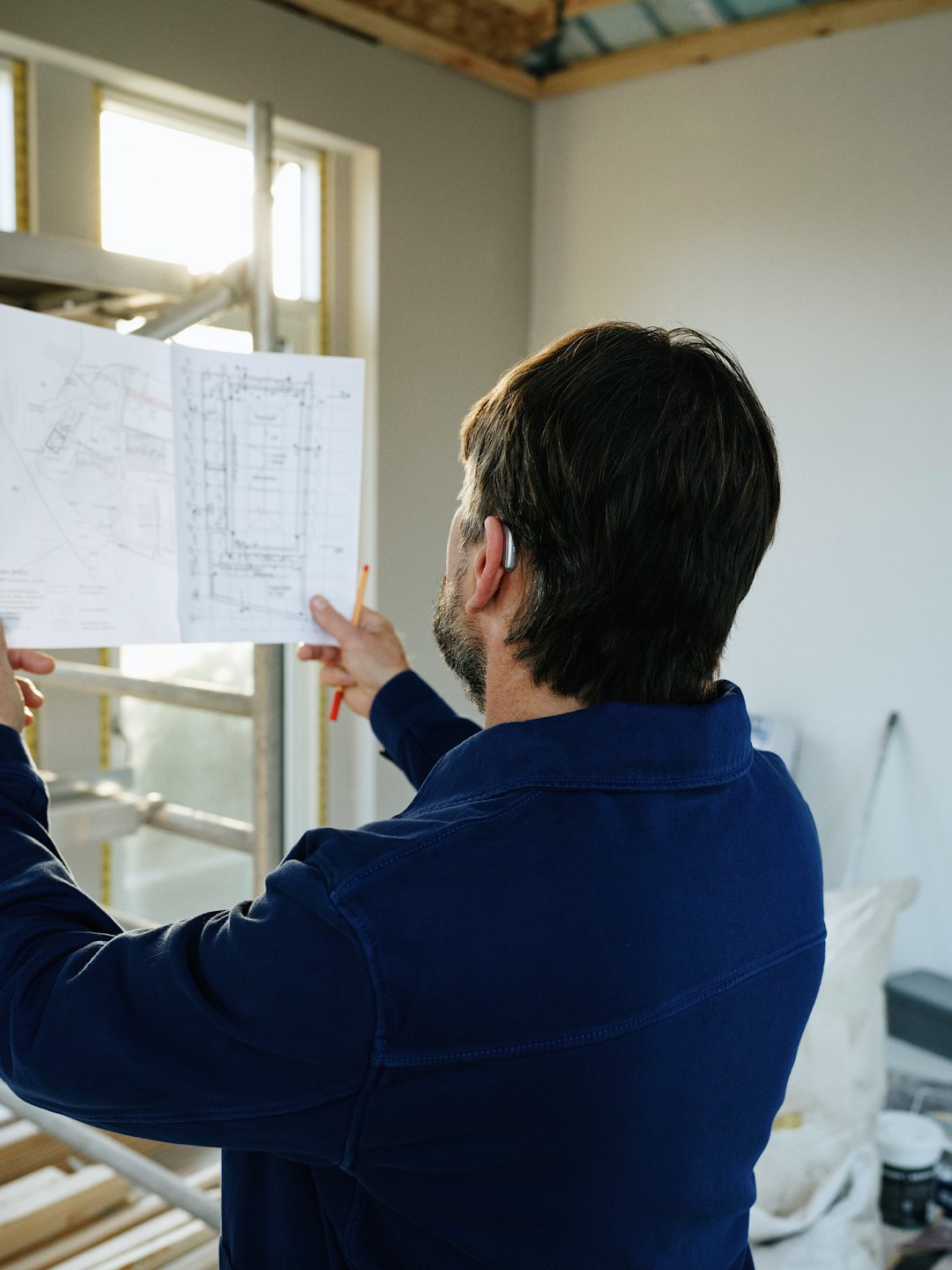 Construction worker reviews blueprints in unfinished room.