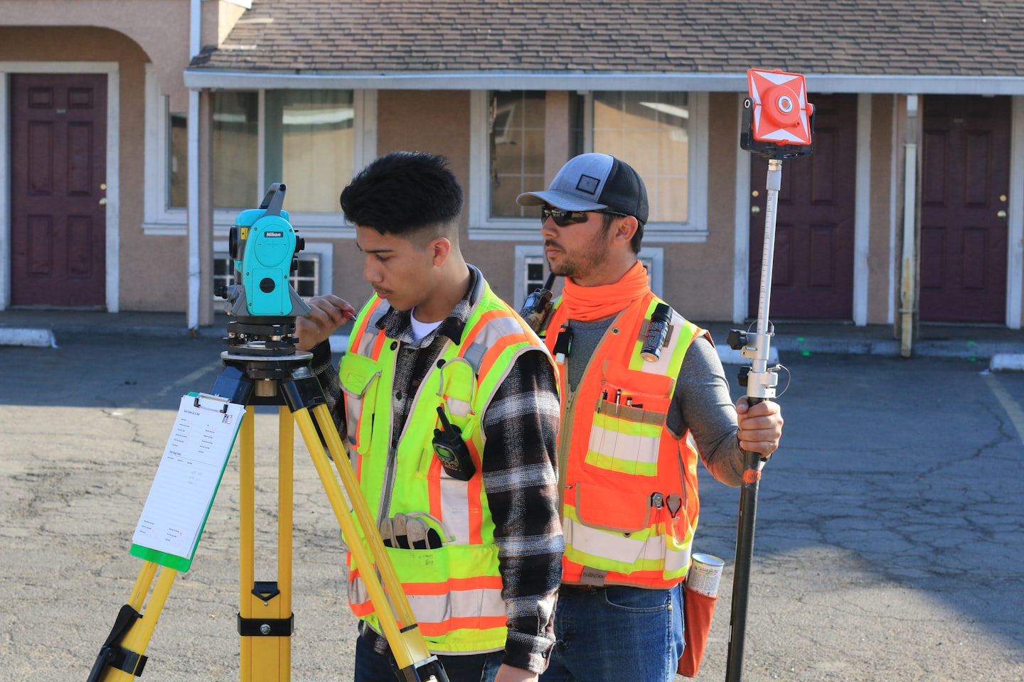 Two surveyors operate a total station and prism pole outdoors.